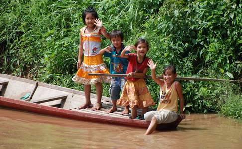 Kinderen zwaaien u vrolijk toe tijdens een boottochtje over de Mekong rivier in Laos